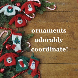 May include: A collection of knitted Christmas ornaments, including a stocking, a snowman sweater, and a wreath sweater. The ornaments are decorated with red, green, and white colors. The text "ornaments adorably coordinate!" is written on a wooden background.
