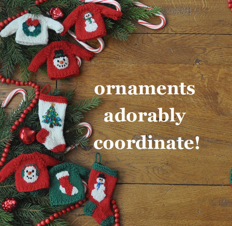 May include: A collection of knitted Christmas ornaments, including a stocking, a snowman sweater, and a wreath sweater. The ornaments are decorated with red, green, and white colors. The text "ornaments adorably coordinate!" is written on a wooden background.