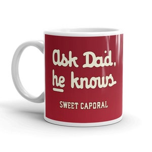 Peut inclure: Une tasse en céramique blanche avec un fond rouge et du texte blanc qui dit "Ask Dad, he knows" et "SWEET CAPORAL" en bas.
