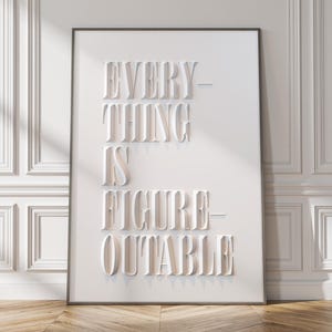 May include: A framed white art print with the words "EVERYTHING IS FIGURE-OUTABLE" in a bold, raised font. The print is set against a white wall with decorative molding and a wooden floor.