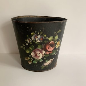Peut inclure: Une poubelle en métal noir avec un motif floral peint sur le côté. Les fleurs sont roses, rouges, jaunes et blanches.