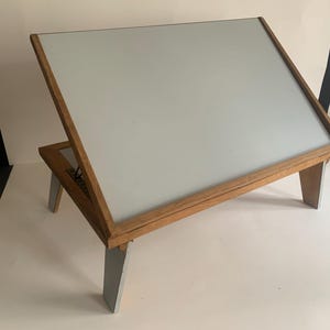 May include: A wooden laptop stand with a white surface and gray legs. The stand is angled for comfortable viewing.