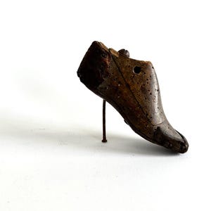 May include: A vintage wooden shoe last, showing signs of age and wear. The shoe form is a dark brown color, with a metal support rod. The last is designed to shape shoes and boots.