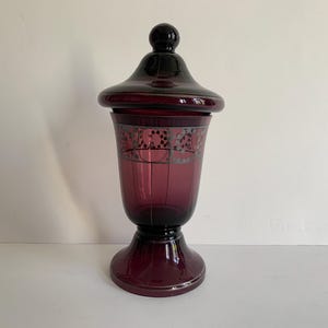 Peut inclure: Un pot à bonbons en verre vintage avec un couvercle. Le pot est de couleur violet foncé avec des motifs gravés argentés. Le couvercle est noir et a un bouton sur le dessus.