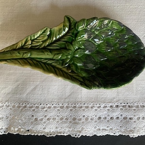 Puede incluir: Un plato de cerámica verde con forma de alcachofa. El plato tiene un diseño detallado con hojas y una superficie texturizada.