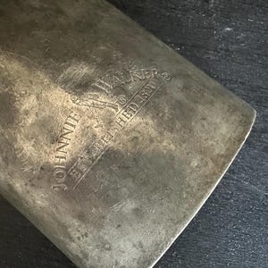 Puede incluir: Primer plano de una superficie met&aacute;lica desgastada con el texto en relieve "JOHNNIE WALKER ESTABLISHED 1820". El metal tiene un aspecto desgastado y envejecido, con ara&ntilde;azos e imperfecciones visibles.