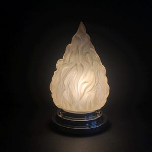 Puede incluir: Una pantalla de lámpara de vidrio blanco con forma de llama con una base de metal plateado.