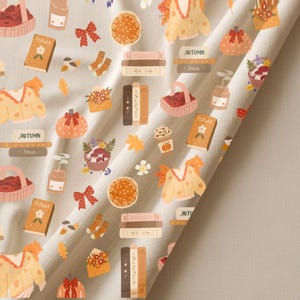 K&ouml;nnte beinhalten: Ein hellbeiger Stoff mit einem sich wiederholenden Muster von herbstlichen Illustrationen. Das Design umfasst K&uuml;rbisse, B&uuml;cher, Pullover, Obstk&ouml;rbe und das Wort "AUTUMN".
