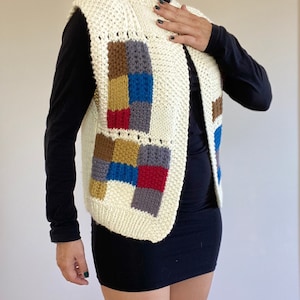 May include: A white knitted vest with a colorful patchwork design. The vest has a V-neck and is made of a soft, chunky yarn.