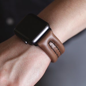 May include: A brown leather watch band with black stitching for an Apple Watch.