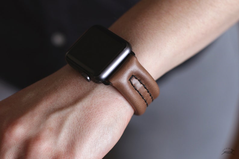 May include: A brown leather watch band with black stitching for an Apple Watch.