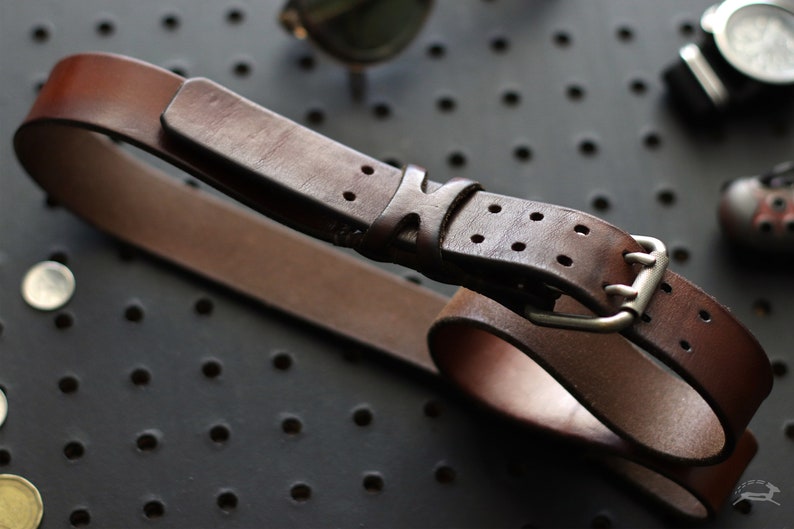 May include: A brown leather belt with a silver buckle and a double-prong design. The belt has a distressed look and is made of high-quality leather.