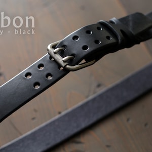 May include: Black leather belt with a silver buckle and multiple rows of holes. The belt is labeled "carbon grey - black".