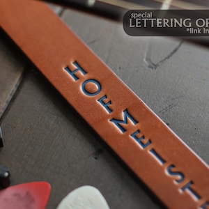 May include: A brown leather guitar strap with the text "HOME-ST" embossed in blue lettering.