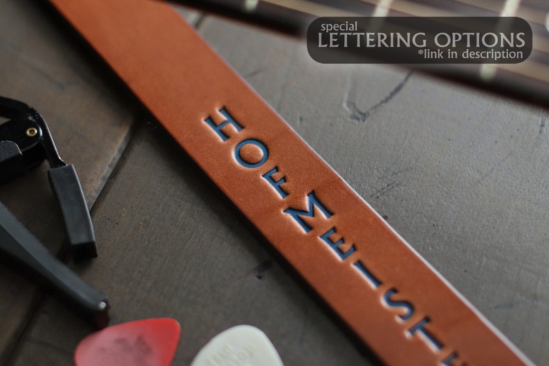 May include: A brown leather guitar strap with the text "HOME-ST" embossed in blue lettering.