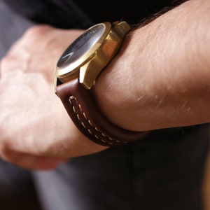 May include: A gold-tone wristwatch with a brown leather band and white stitching. The watch has a black face.