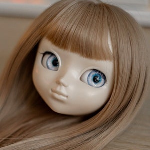 May include: A doll with long, straight, light brown hair and blue eyes. The doll is wearing a white wig.