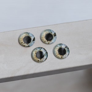 Op de afbeelding: Vier plastic poppenogen met zwarte pupillen en blauwe, groene en gele iris.