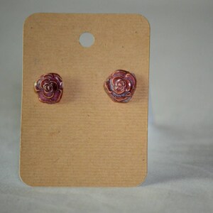 May include: A pair of rose-shaped stud earrings with a brown and purple glaze.