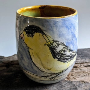 May include: A ceramic mug with a hand-painted design of a yellow bird with black markings on a blue and white background.