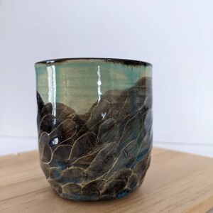Puede incluir: Una taza de cerámica con un esmalte azul oscuro y marrón. El esmalte tiene un patrón texturizado en forma de onda.