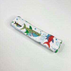 May include: A rolled-up white baby blanket featuring colorful cartoon sharks, fish, and bubbles. The sharks are in shades of blue, green, and red. The blanket has a green trim.