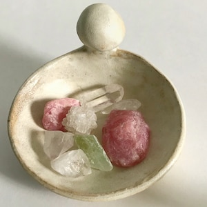 May include: A white ceramic dish with a raised handle, containing a variety of pink, clear, and green crystals.
