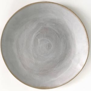 May include: A white ceramic plate with a subtle swirl pattern. The plate has a light brown rim.