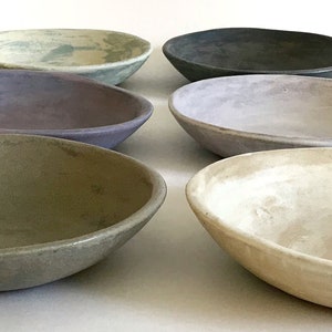 May include: Six ceramic bowls in various shades of gray, green, and purple. The bowls are all oval-shaped and have a slightly textured surface.