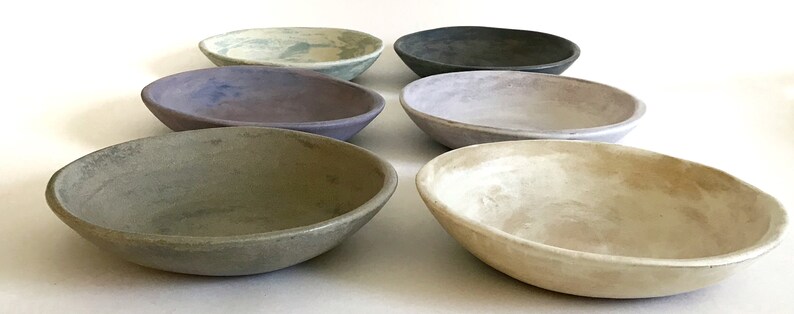May include: Six ceramic bowls in various shades of gray, green, and purple. The bowls are all oval-shaped and have a slightly textured surface.