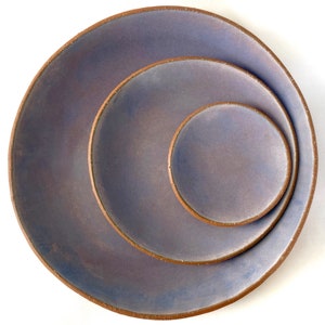 May include: Three ceramic plates nested together. The plates are a light purple color with a brown rim. The plates are all different sizes.