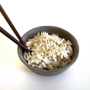 May include: A close-up of a bowl of white rice with two wooden chopsticks on the side.