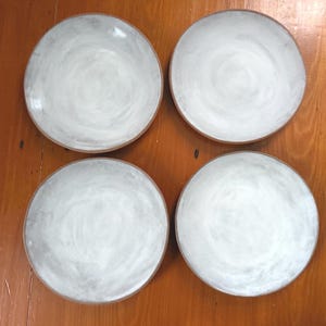 May include: Four round ceramic plates with a white and gray swirl design. The plates have a brown rim and are arranged in a square formation. The plates are suitable for serving food.