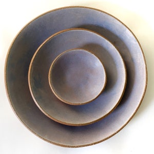 May include: Set of three ceramic bowls in shades of purple and brown. The bowls are nested inside each other, with the smallest bowl at the top.
