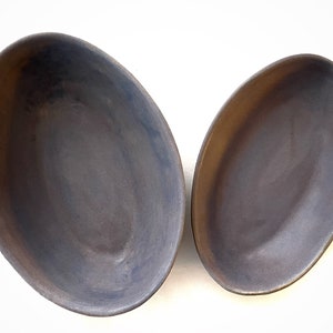 May include: Two oval ceramic bowls, one larger than the other, both with a dark gray glaze. The bowls are slightly textured and have a subtle sheen.