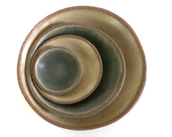 May include: Set of three ceramic bowls in various shades of brown and green. The bowls are nested inside each other, with the smallest bowl in the center.