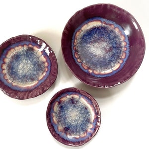 May include: Three ceramic bowls with a purple glaze and a blue and white crackle glaze design. The bowls are nested inside each other, with the largest bowl on the bottom and the smallest bowl on top.