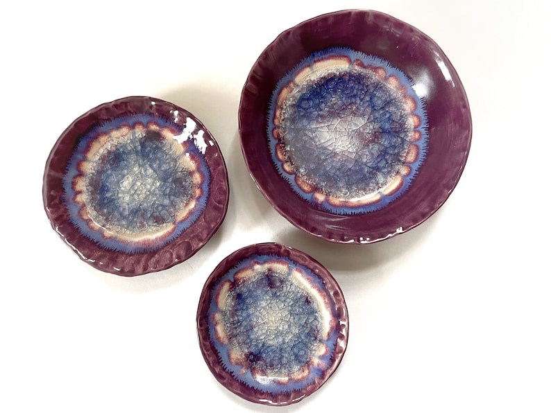 May include: Three ceramic bowls with a purple glaze and a blue and white crackle glaze design. The bowls are nested inside each other, with the largest bowl on the bottom and the smallest bowl on top.