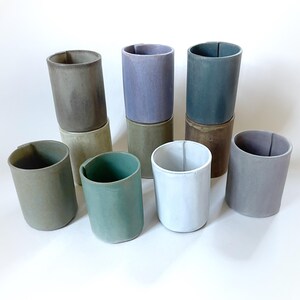 May include: Set of ten ceramic cups in various shades of green, brown, purple, and white. The cups are stacked in pairs, with the top cup of each pair being a different colour than the bottom cup.