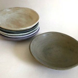 May include: A stack of five ceramic bowls in various shades of green, purple, and white. The bowls are all slightly different sizes and have a rustic, handmade look.