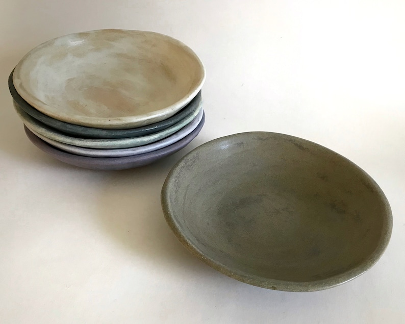 May include: A stack of five ceramic bowls in various shades of green, purple, and white. The bowls are all slightly different sizes and have a rustic, handmade look.