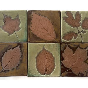 May include: A set of six square ceramic tiles arranged in two rows. Each tile features a distinct embossed leaf impression in a reddish-brown tone. The background glazes alternate between a muted sage green and a deep, glossy chocolate brown.