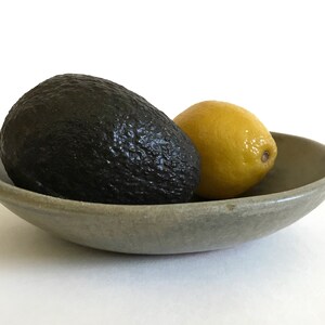 May include: A green ceramic bowl with a dark green avocado and a yellow lemon inside.