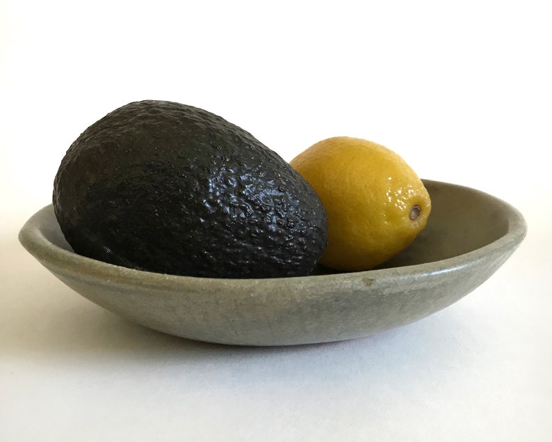 May include: A green ceramic bowl with a dark green avocado and a yellow lemon inside.