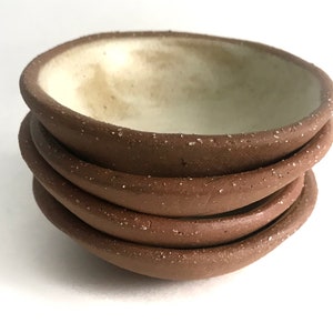 May include: A stack of four small, brown ceramic bowls with a speckled texture. The bowls have a white interior.