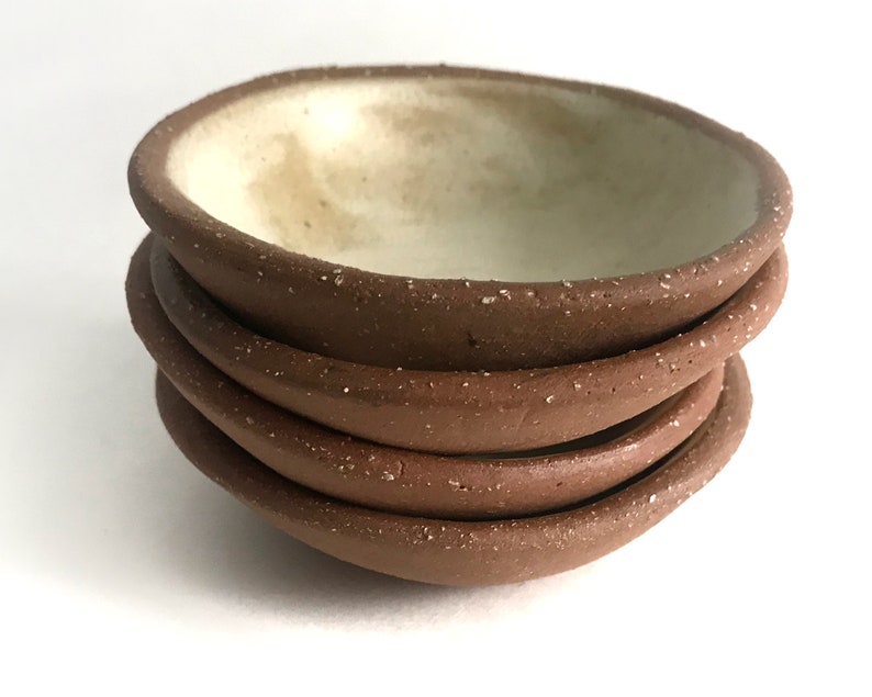 May include: A stack of four small, brown ceramic bowls with a speckled texture. The bowls have a white interior.