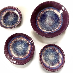 May include: Set of four purple ceramic bowls with a crackle glaze and a blue and white design. The bowls are of varying sizes.