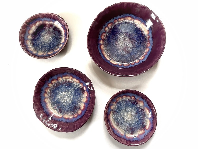 May include: Set of four purple ceramic bowls with a crackle glaze and a blue and white design. The bowls are of varying sizes.