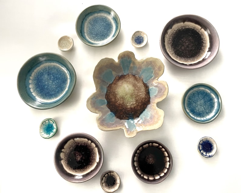 May include: Assortment of small ceramic dishes in various shades of blue, green, and brown with a speckled glaze. The dishes are arranged in a circle on a white background.