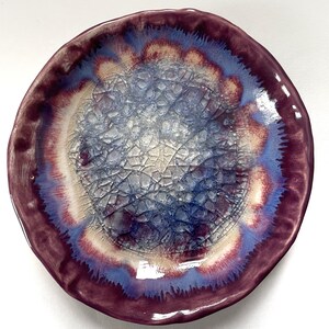 May include: A ceramic plate with a crackled glaze in shades of purple, blue, and white. The plate has a scalloped edge and a unique, organic design.